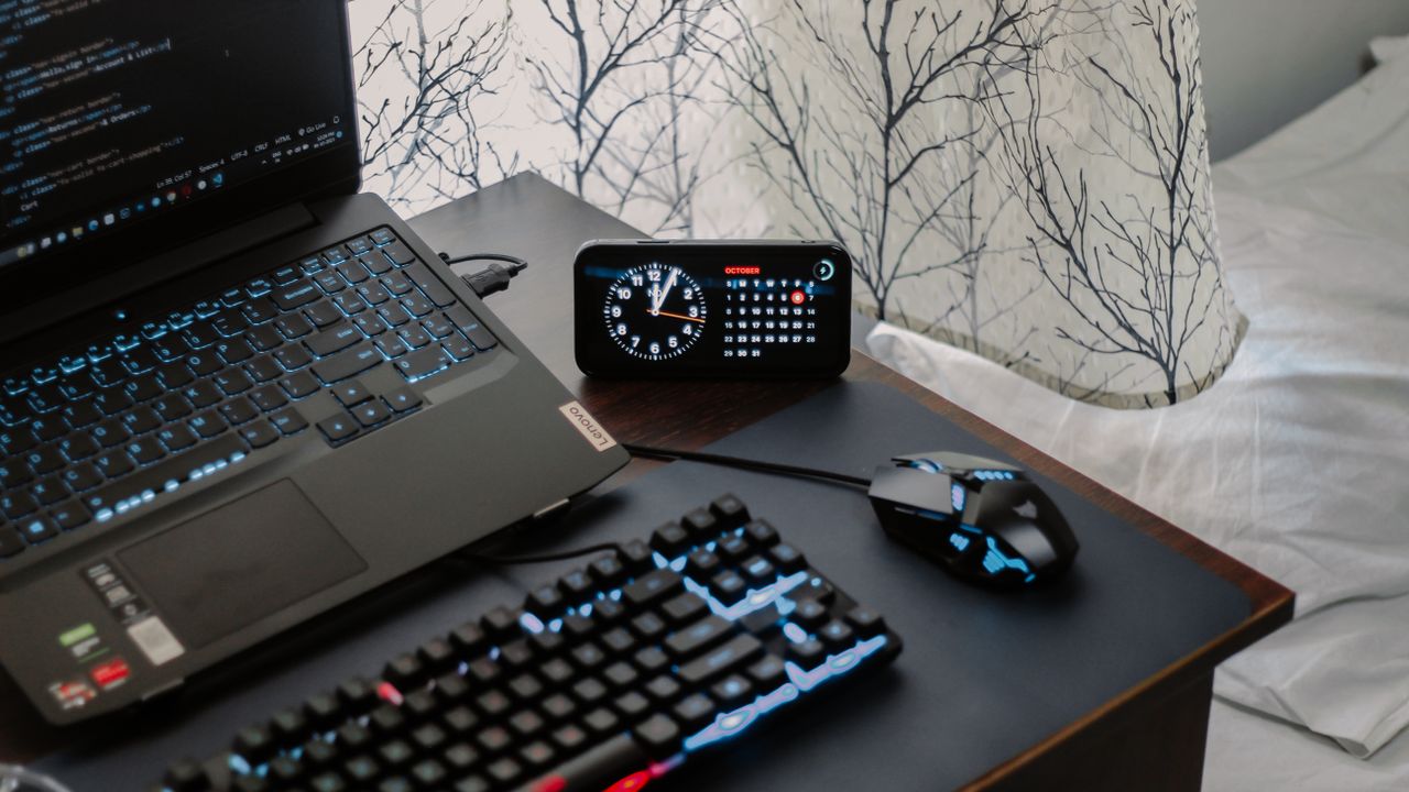 A modern workspace featuring a laptop, digital clock, gaming mouse, and keyboard, ideal for work and tech enthusiasts.