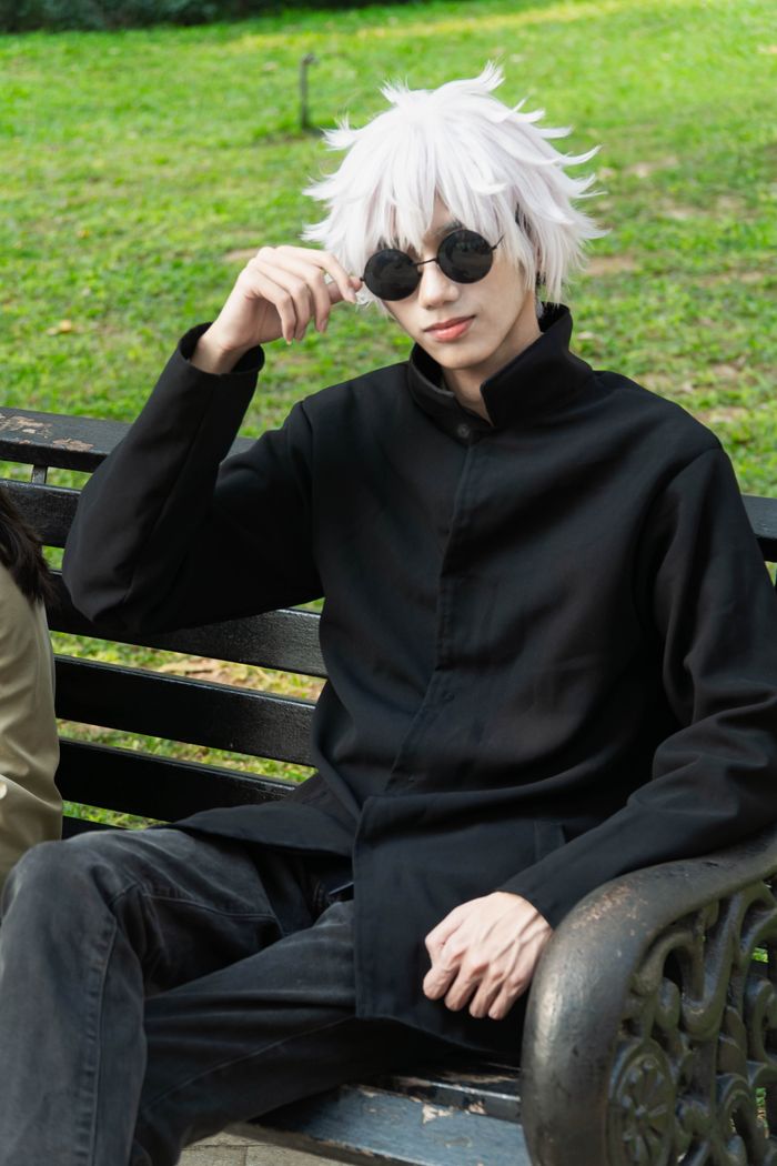 Person in black coat and sunglasses sitting on a park bench in a sunny setting.